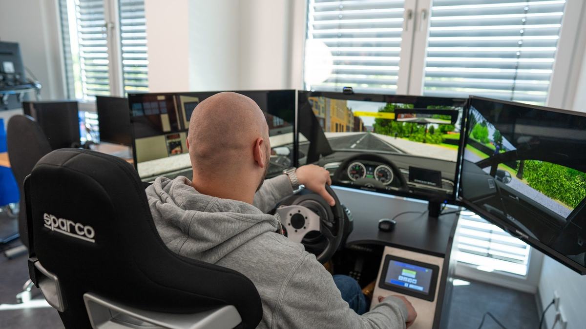 Im Vordergrund Fahrlehrer, der positiv Geste zeigt, im Hintergrund lächelnde Fahrschülerin, beide im Auto